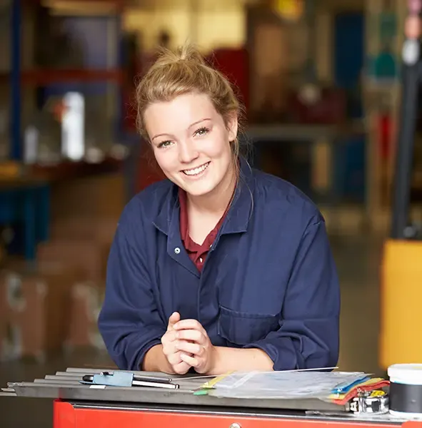 Tradesperson in work coveralls leaning on a tool bench in her shop