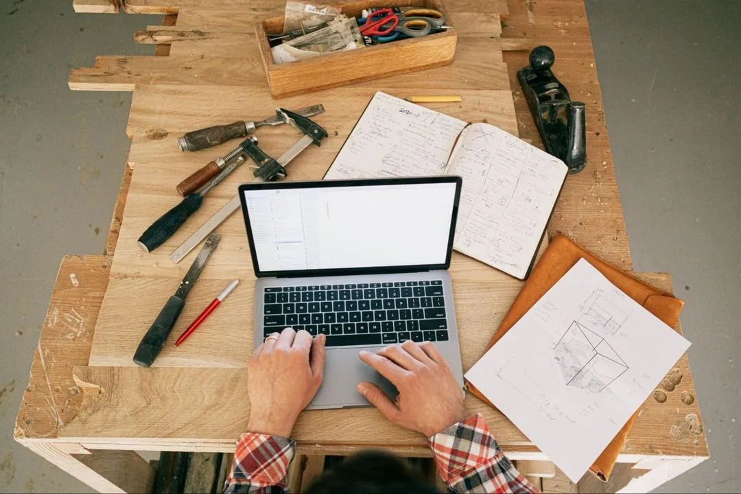 A construction worker reviews documents on a laptop on a job site.